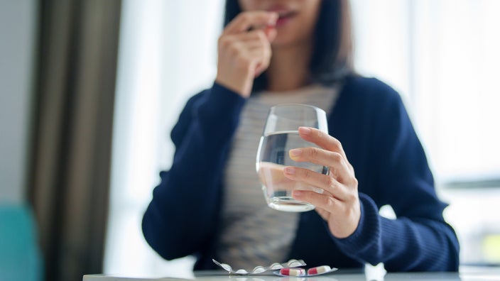 A woman prepares to take her medication while holding a glass of water.
