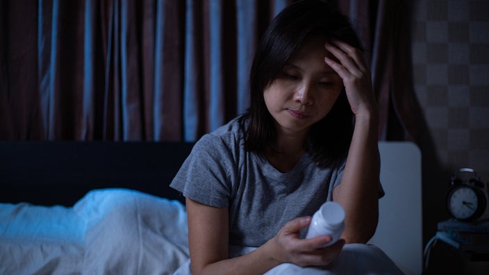 A woman who is having trouble sleeping holds a prescription bottle of pills as she sits in bed.