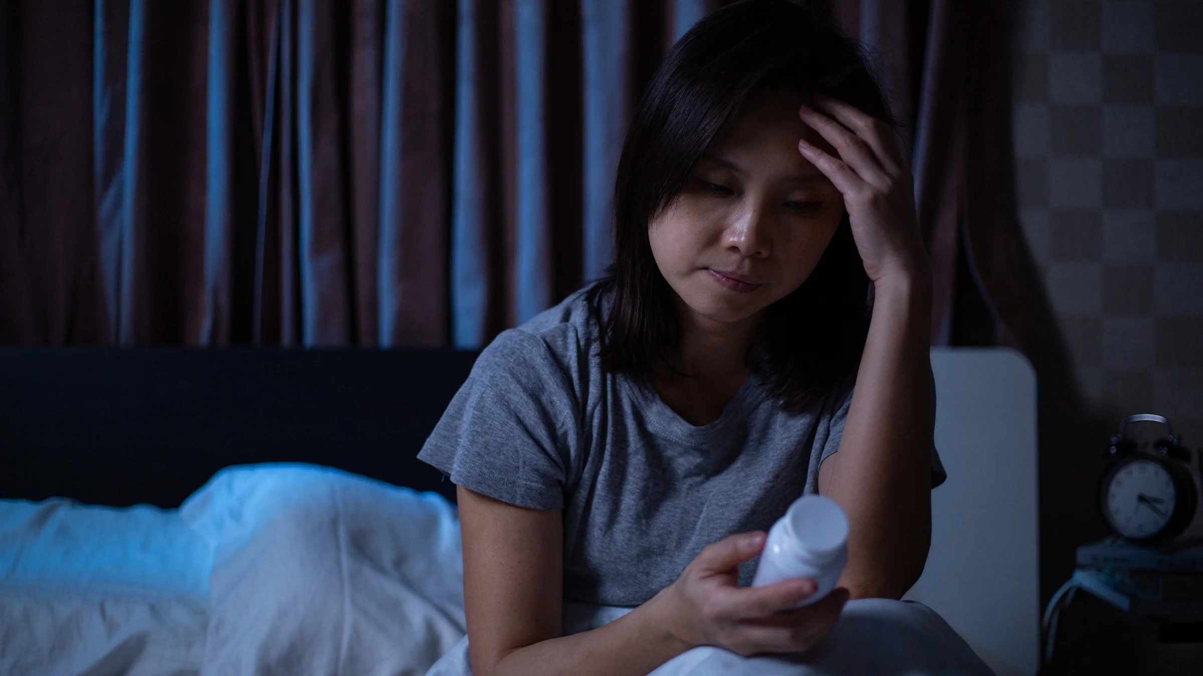 A woman who is having trouble sleeping holds a prescription bottle of pills as she sits in bed.