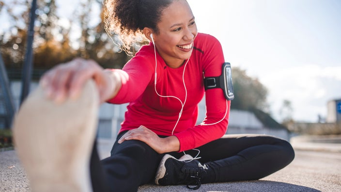 Woman doing hamstring stretches after an outdoor run. She is wearing white ear bud headphone.