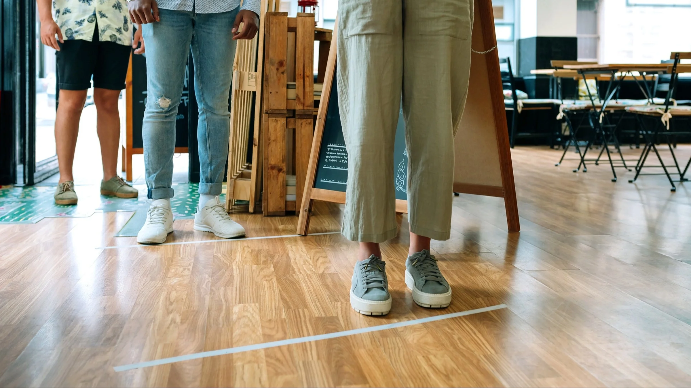 Cropped shot of people's legs and feet as they stand six feet apart waiting at a restaurant.