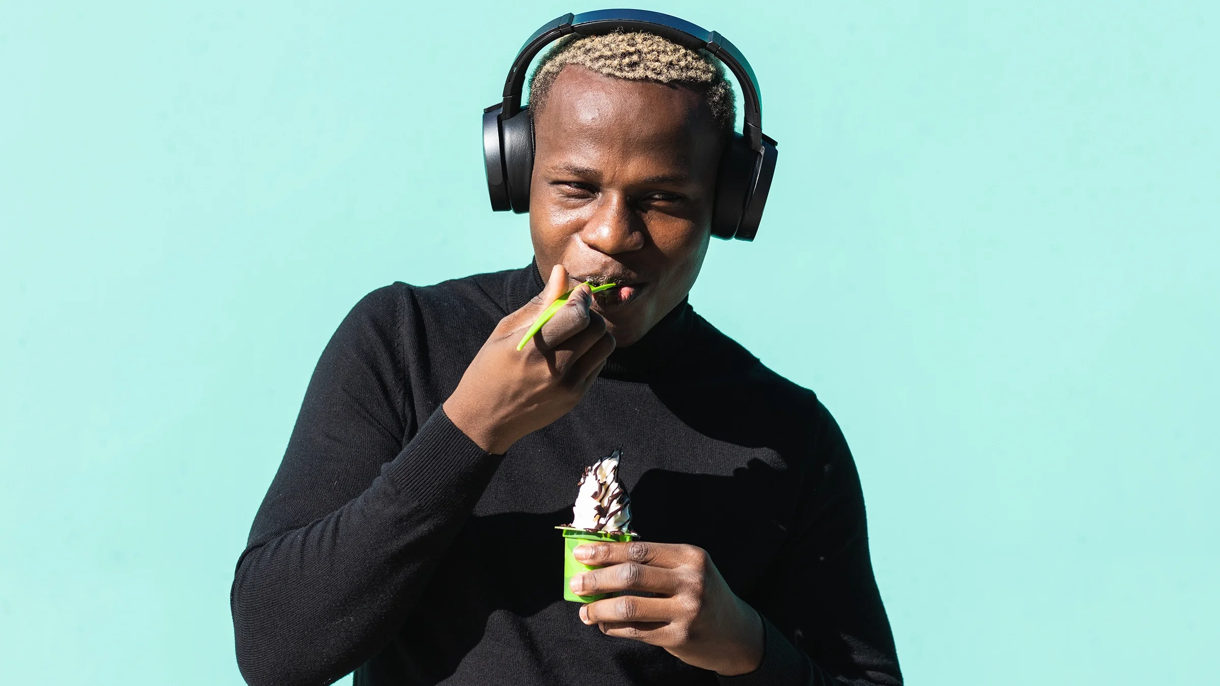 A man wearing headphones eats a spoonful of soft serve.