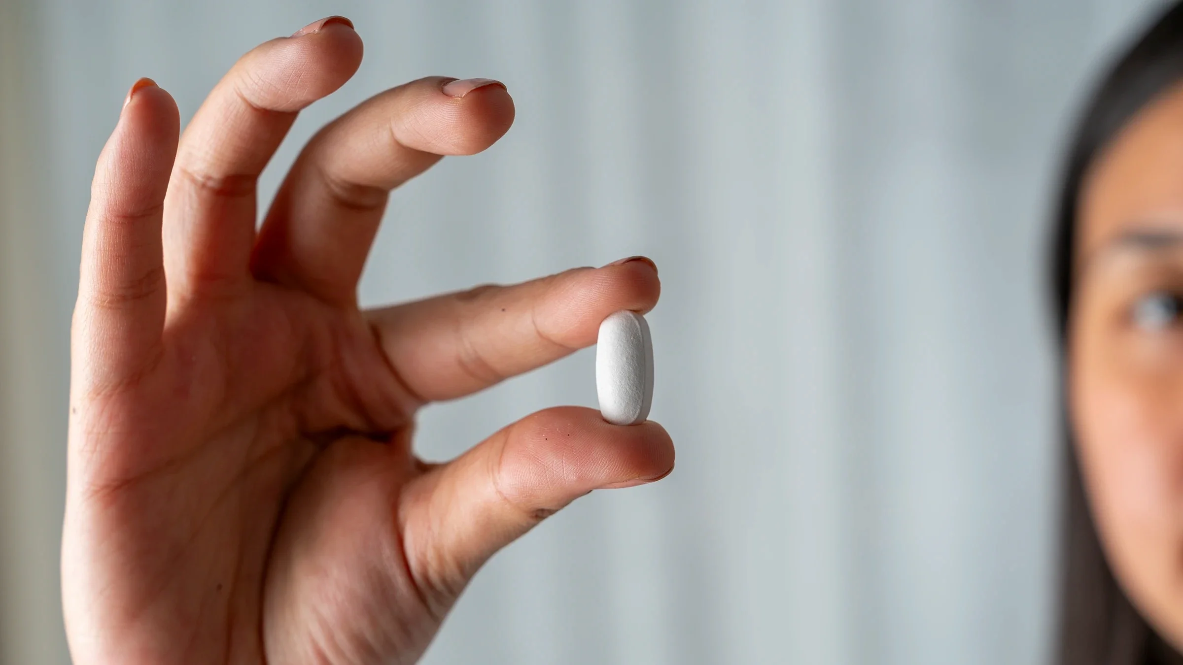A woman holds a pill tablet between her thumb and forefinger.