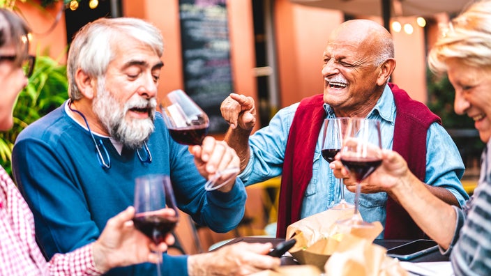 Group of senior friends enjoying dinner and wine while laughing.
