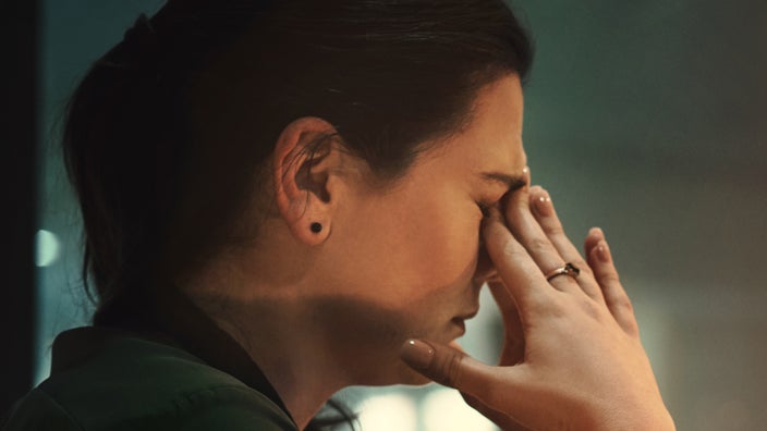 Close-up of a woman rubbing her eyes in a dark room.
