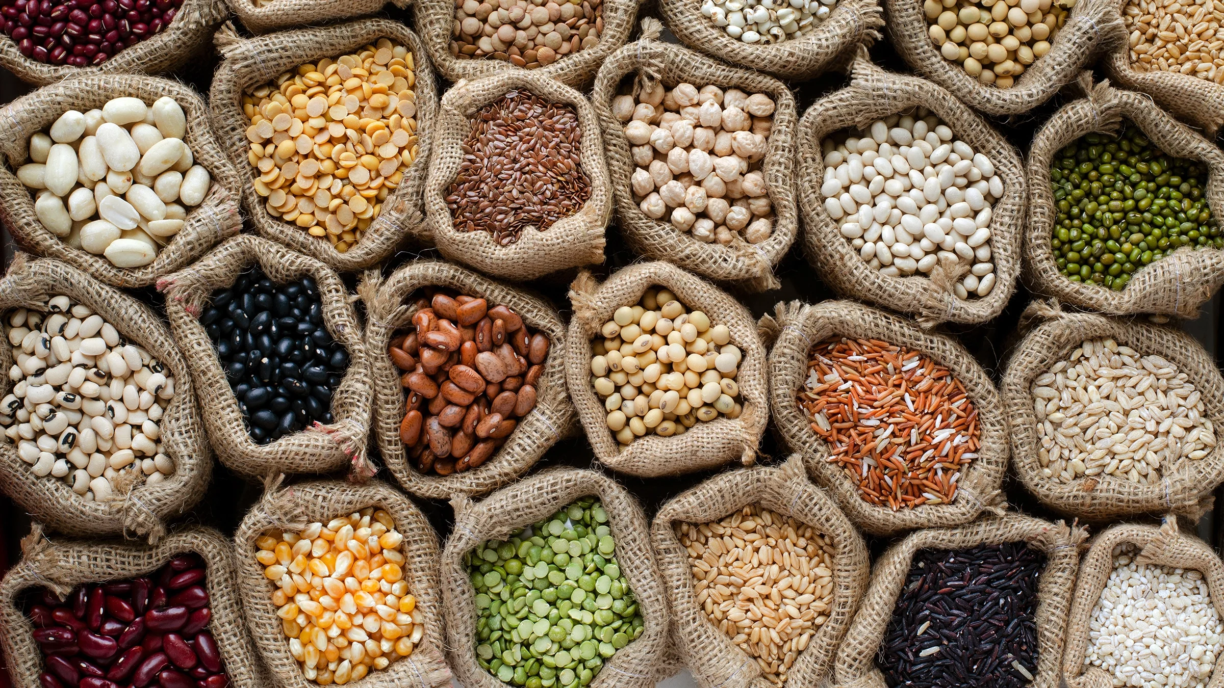 Top down view of various beans, seeds, grains, and legumes in burlap bags.