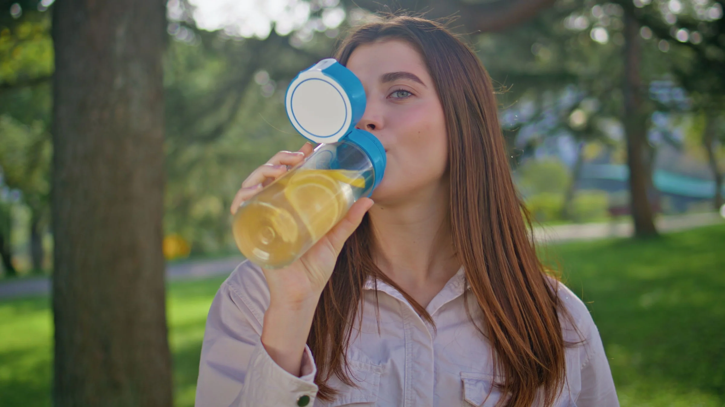 A person drinking a bottle of lemon water in a park.