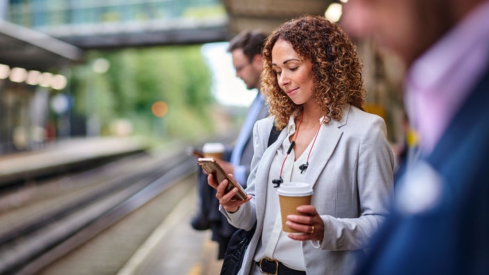 A woman reads on her cell phone while waiting on a train platform.