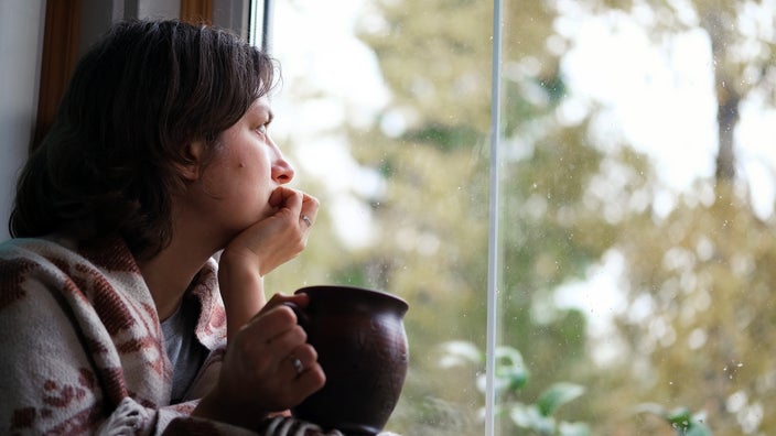 A woman sits near the window in a melancholy mood.