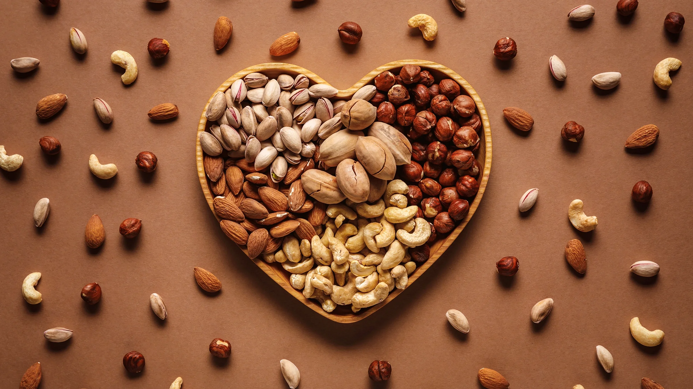 Flat lay with a heart-shaped box, and assorted nuts on a brown tabletop.
