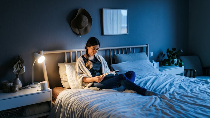 Woman reading a book in bed, in the dark, with the bedside light on.