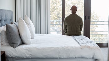 depression: mental health: man sitting on edge of bed back to camera-1202259514