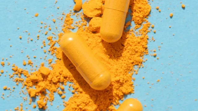 Supplements and herbs: Turmeric: yellow powder capsule pills on blue background-1308865960