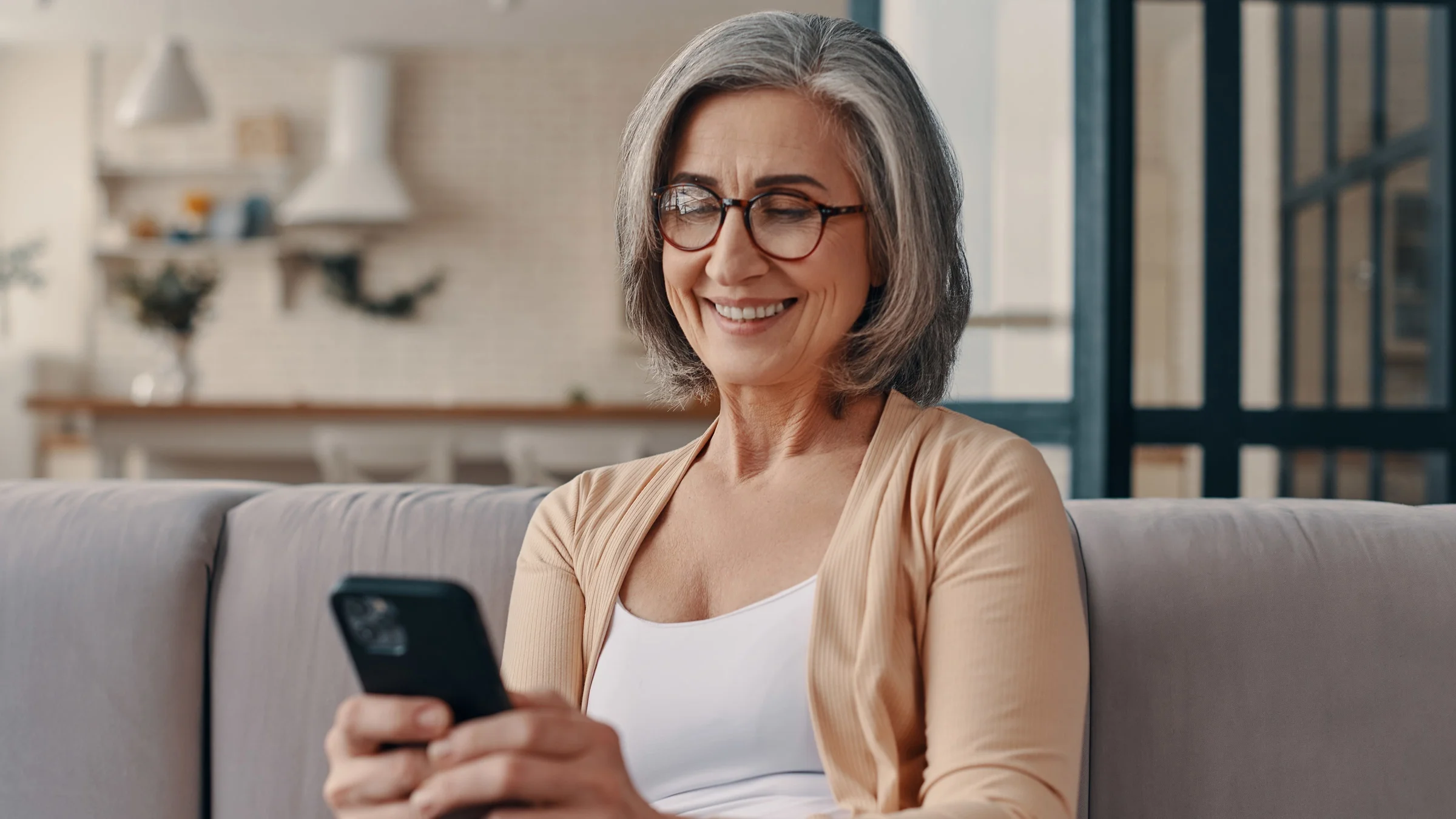 Photo of a senior woman sitting on the couch, she is looking at her smartphone.