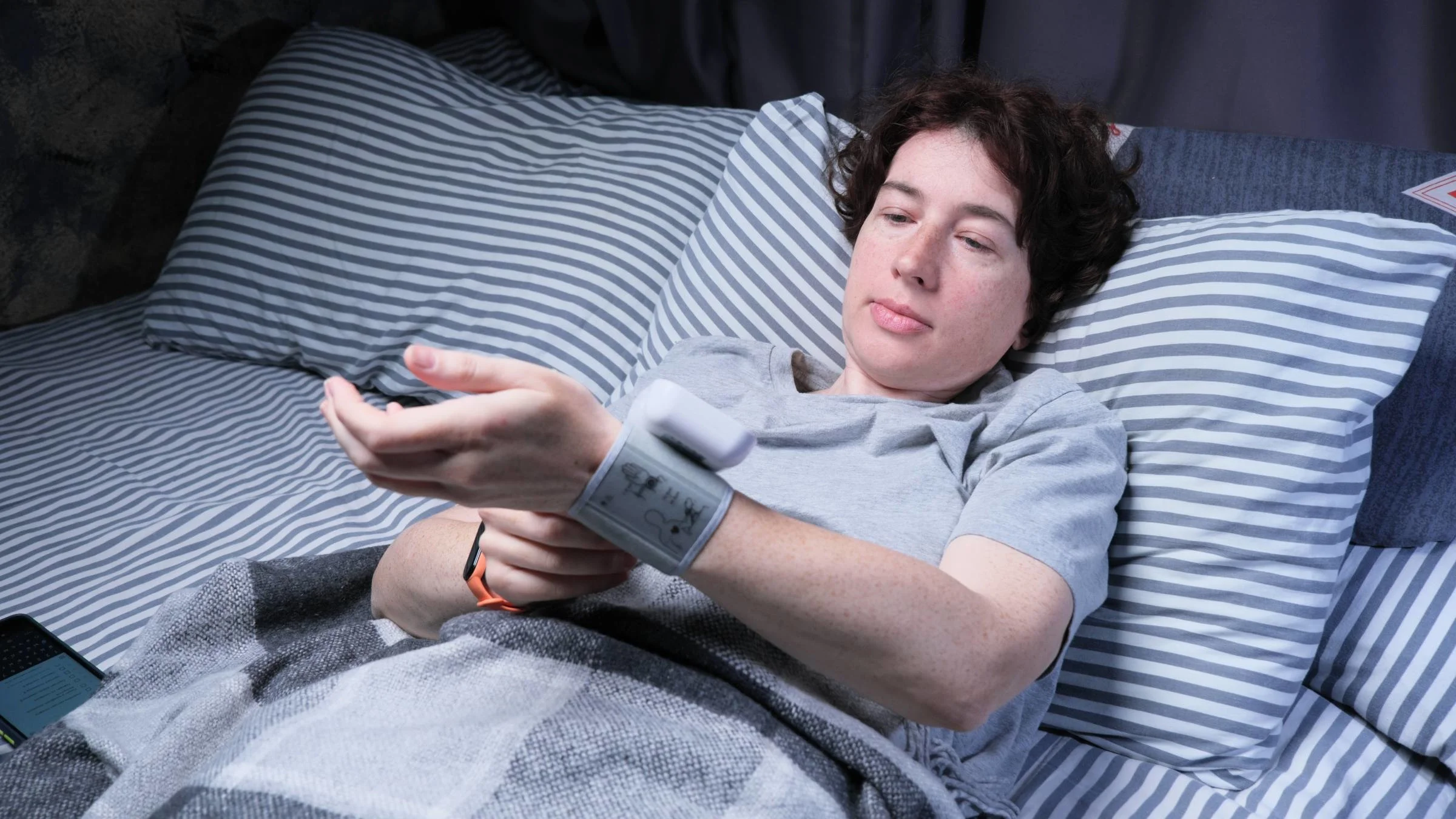 A sick person taking their blood pressure in bed.