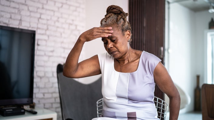 An older woman is sitting down with her hand on her forehead. She looks like she is lightheaded and dizzy.