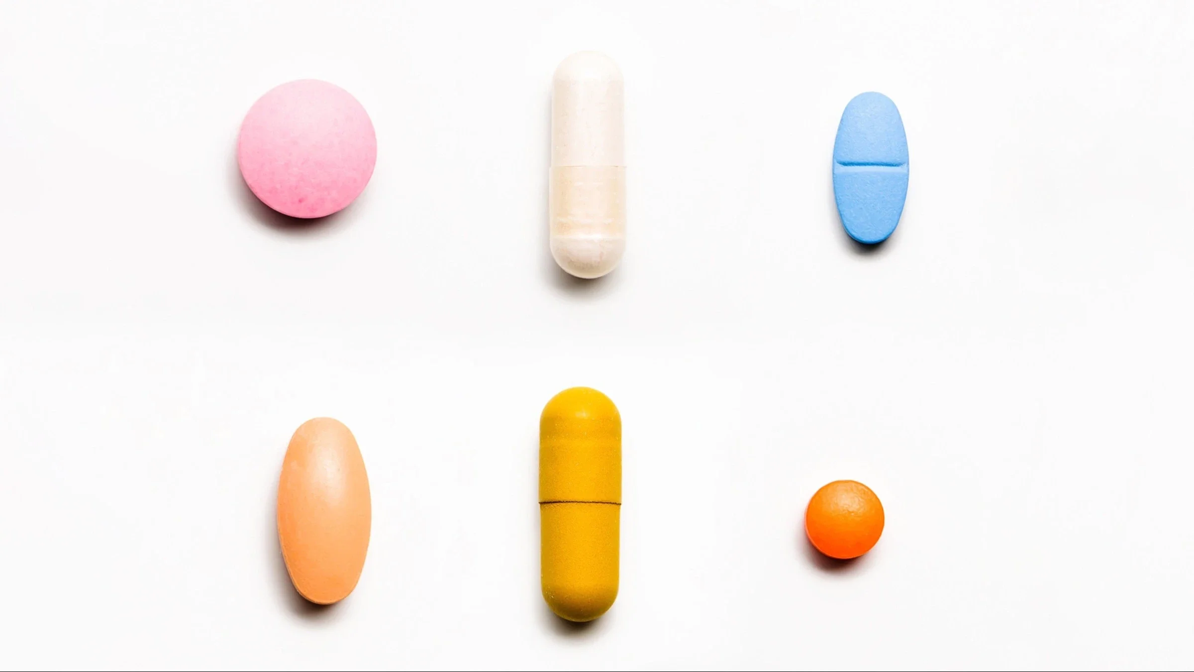 Six colorful pills of various shapes on a white background.