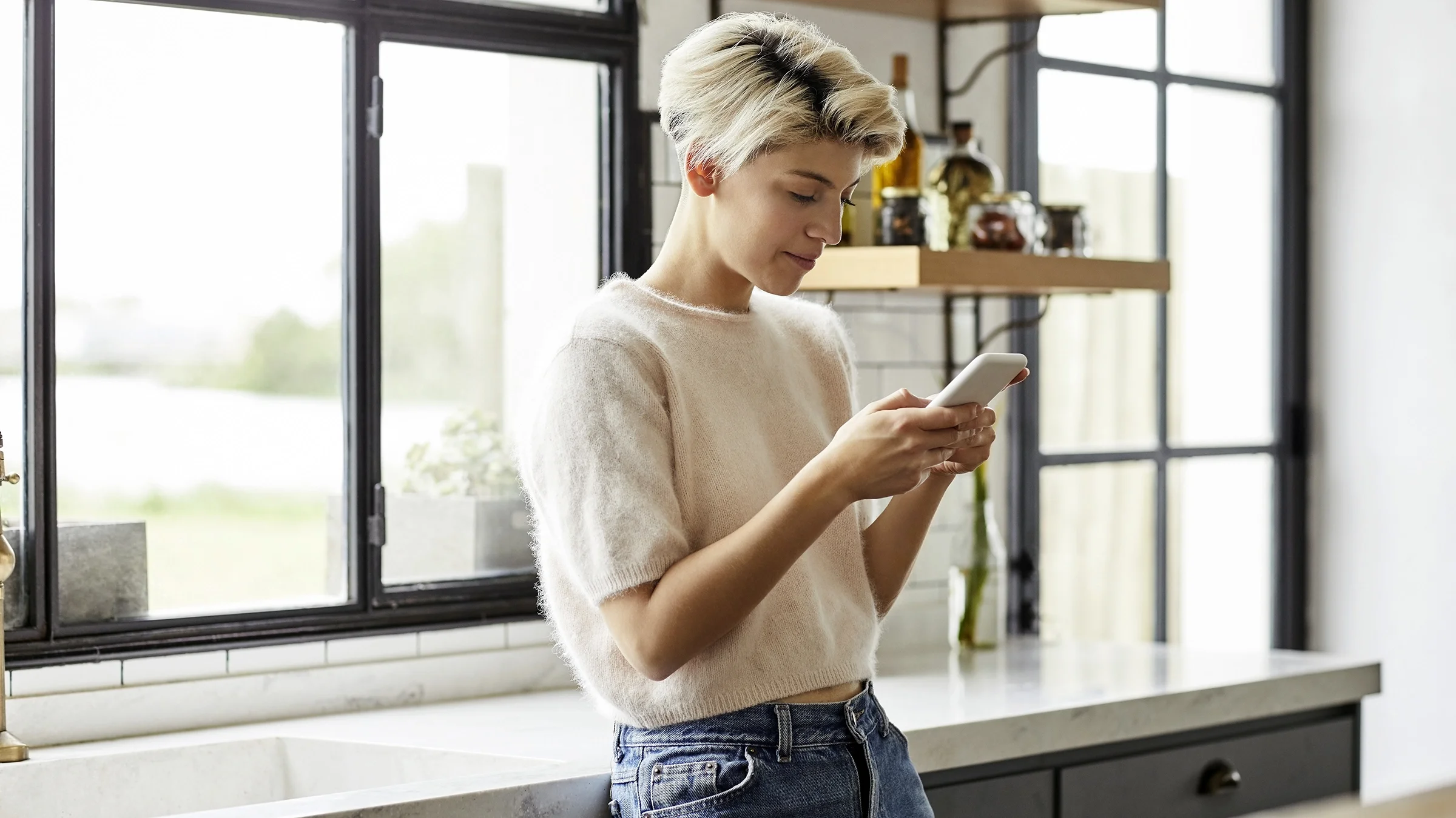Smiling woman in kitchen using her smart phone.