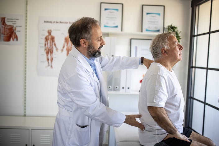 Elderly male patient having his doctor check out his lower back in an exam room.