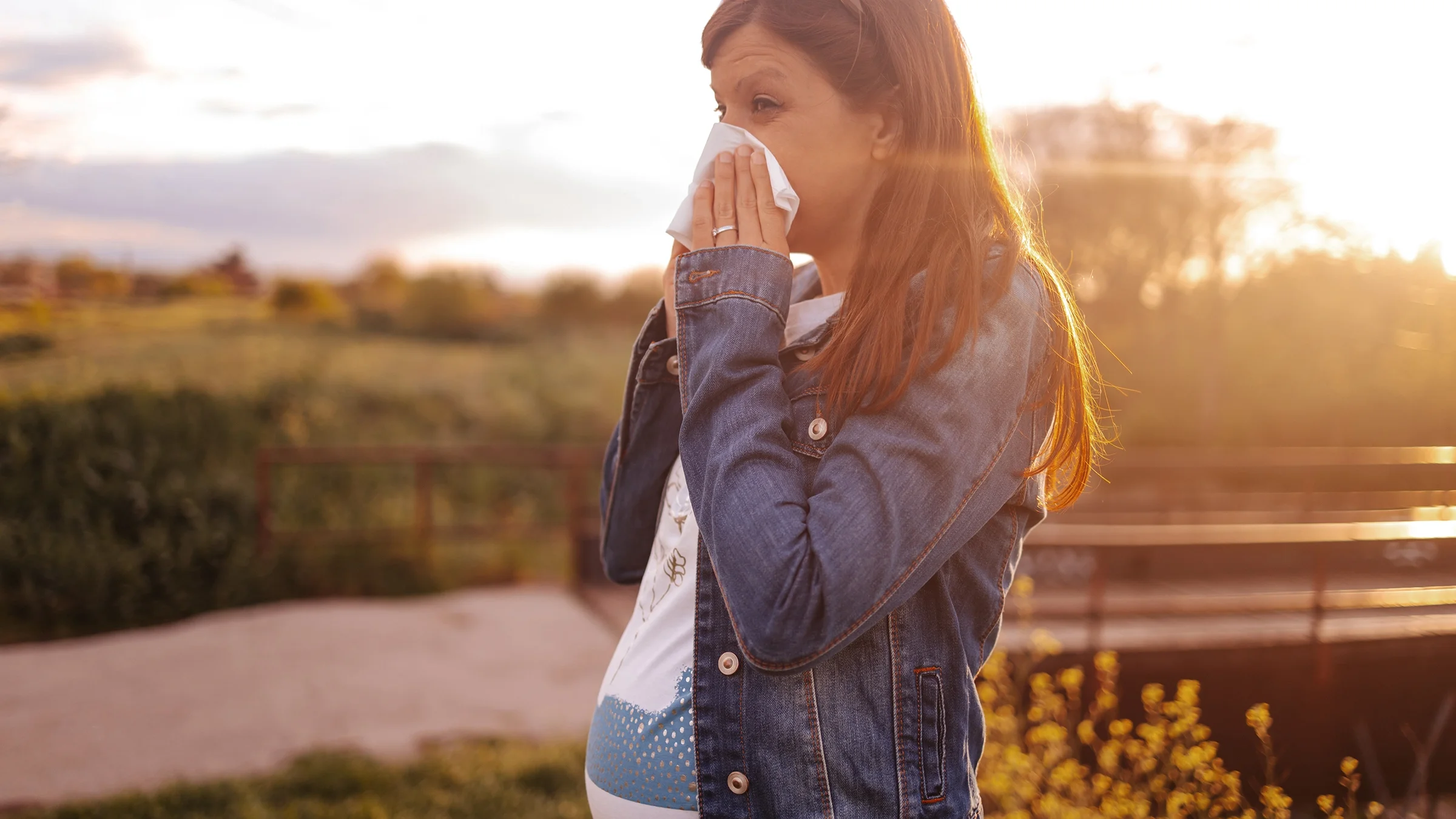 A pregnant woman blows her nose while outdoors.