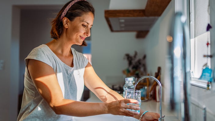 A woman fills a glass with water from the tap.