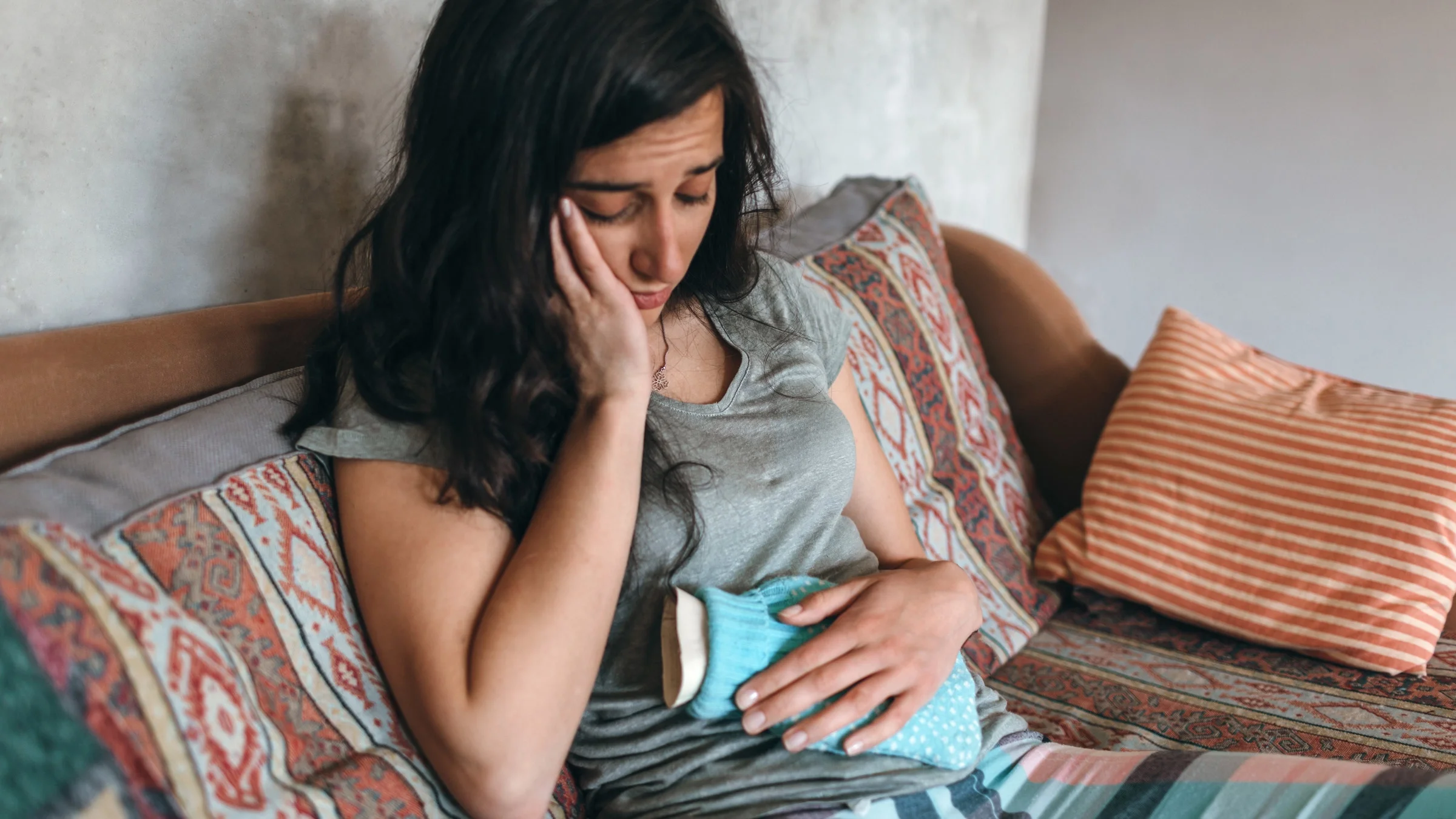 A person sitting on their couch in pain, holding a water bottle.