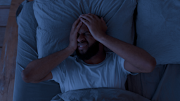 A man clutches his head in pain as he suffers from a migraine in bed at night.
Prostock-Studio/iStock via Getty Images Plus