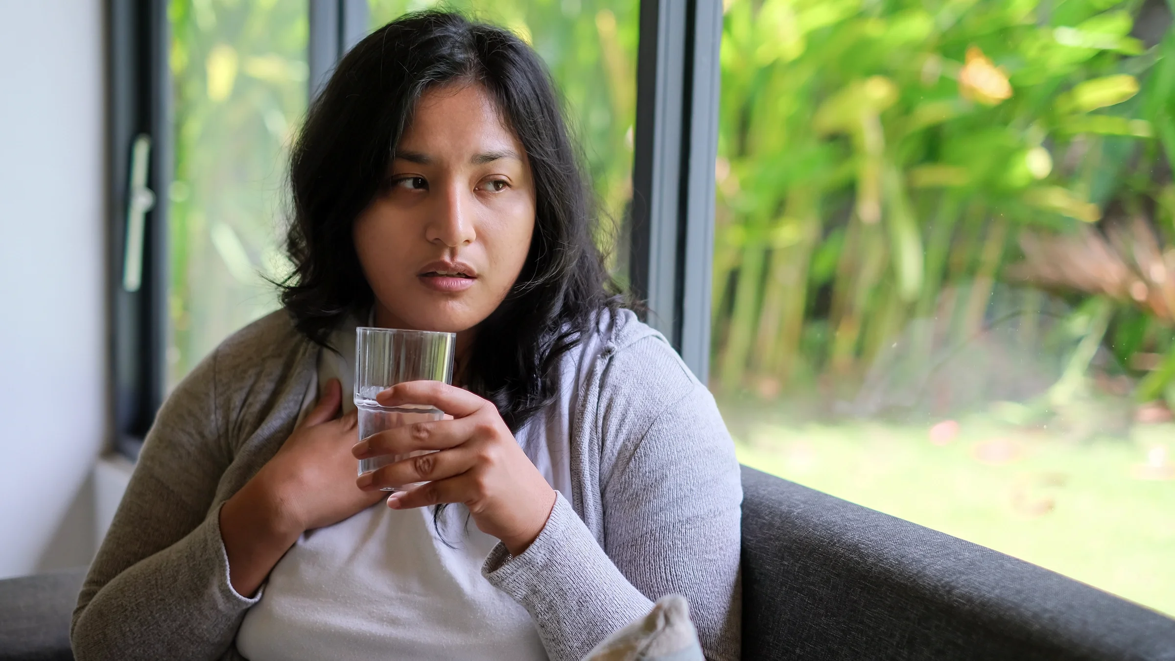 Woman drinking a glass of water while sitting on a sofa.