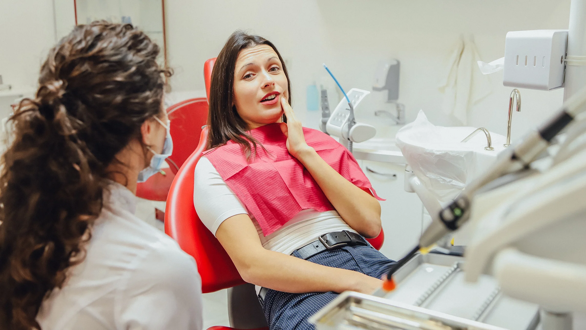 A dentist is consulting with a patient who is rubbing their cheek from gum pain.