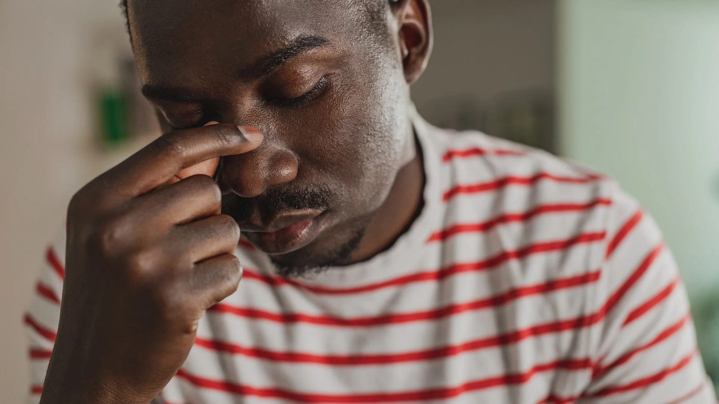 Close-up of a man looking worried and sad with his fingers on the bridge of his nose.