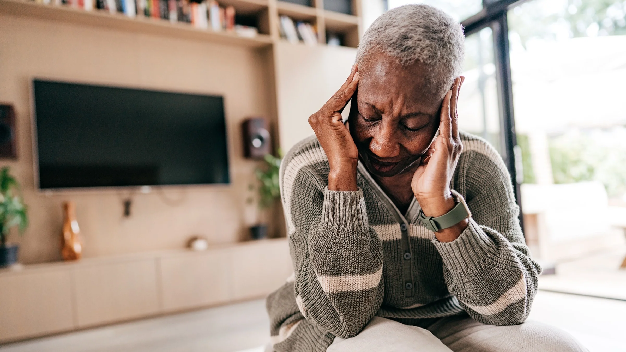 Older woman feeling severe headache pain. She has both hands on her temples rubbing her head in pain.