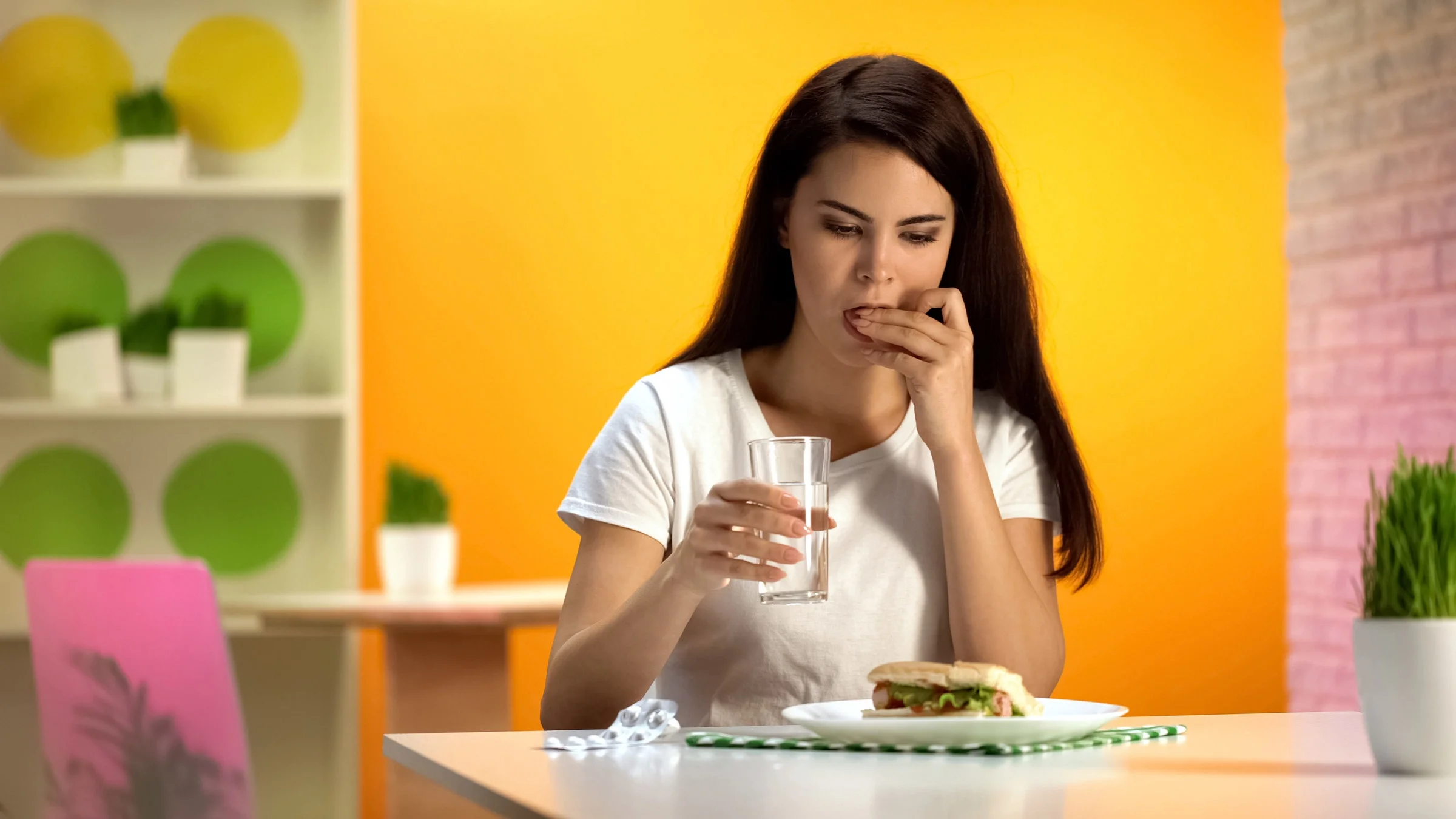 A person taking a pill before eating a sandwich.