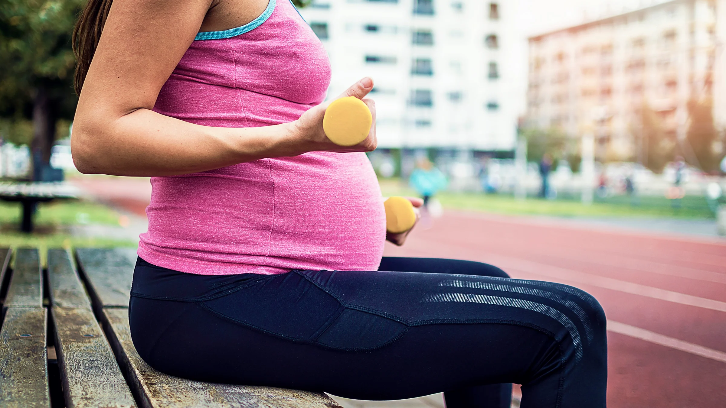 Cropped close-up shot of a pregnant woman working out at the public track and field.