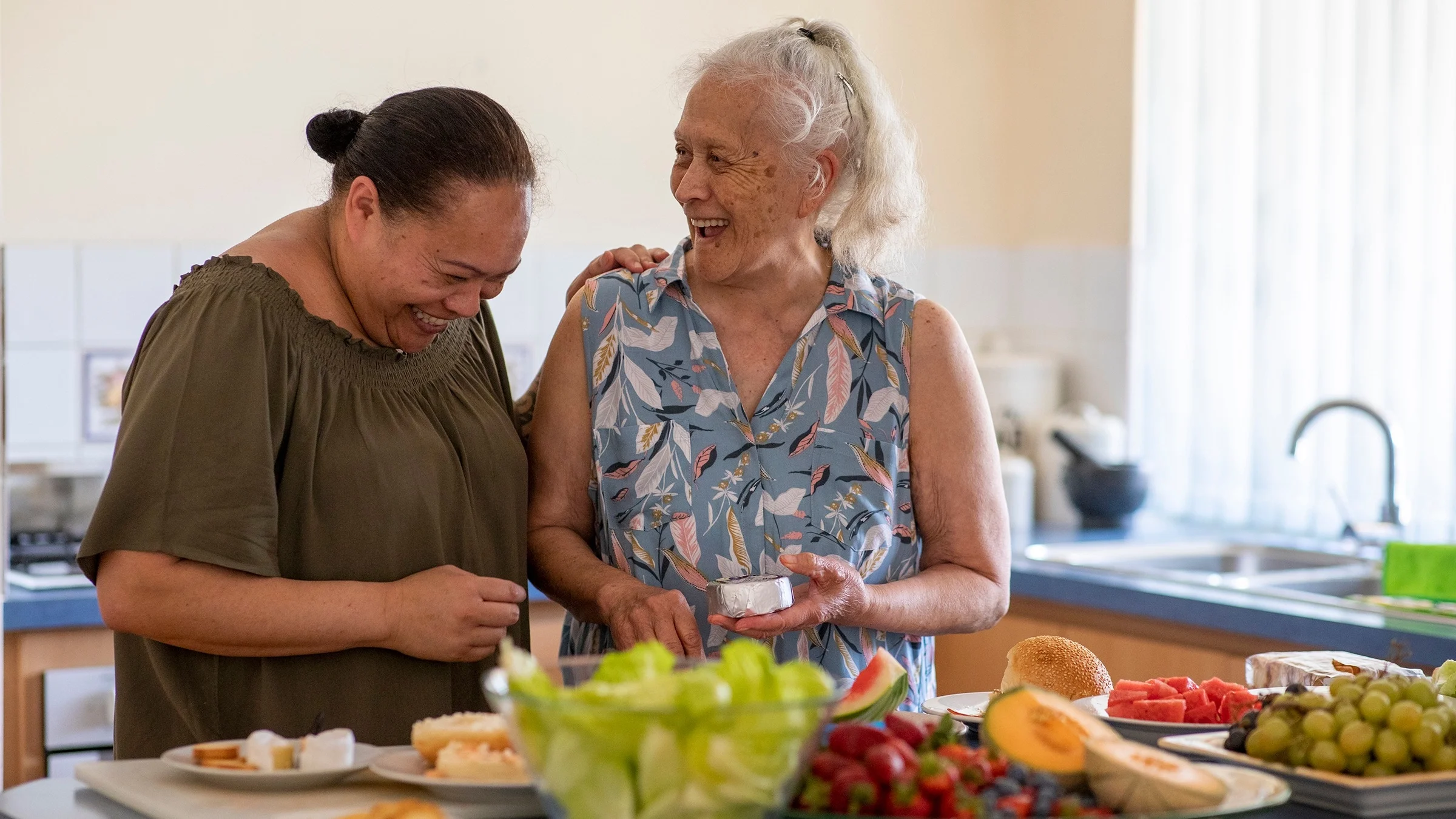 Elderly mother and her daughter smiling a cooking in the kitchen.
