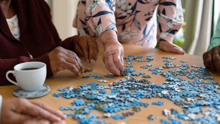 Close-up of a few older people doing a puzzle together. The focus is on the puzzle pieces and their hands.