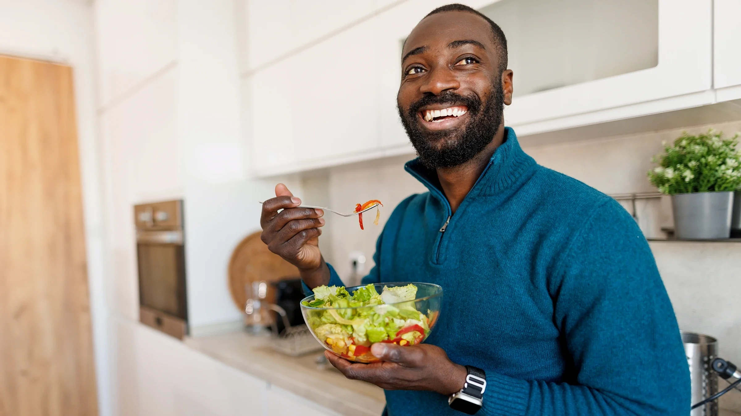 A man eats a salad in the kitchen.