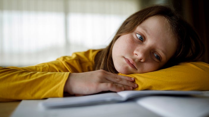 Young girl with long hair resting and looking bored while studying at home.