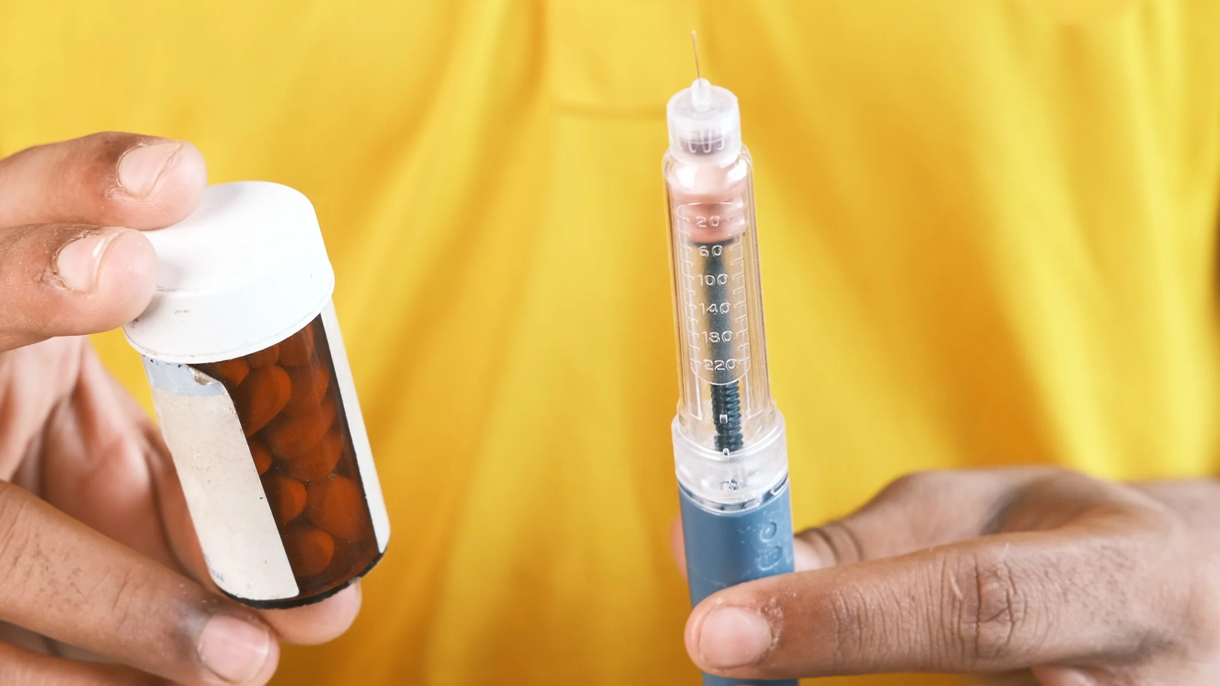 Close-up of someone holding an insulin pen and a pill bottle.