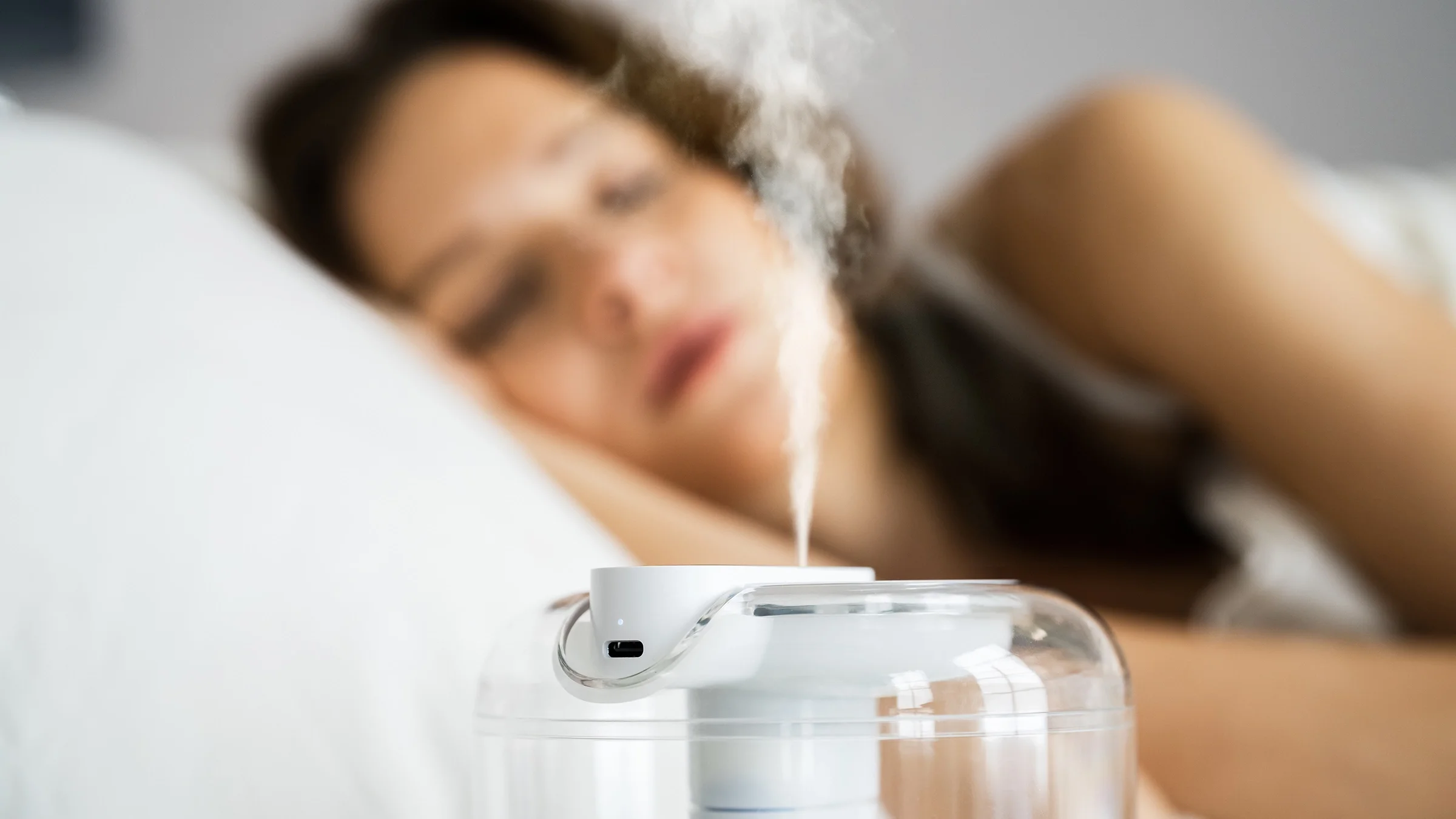 A woman is sleeping next to a humidifier.