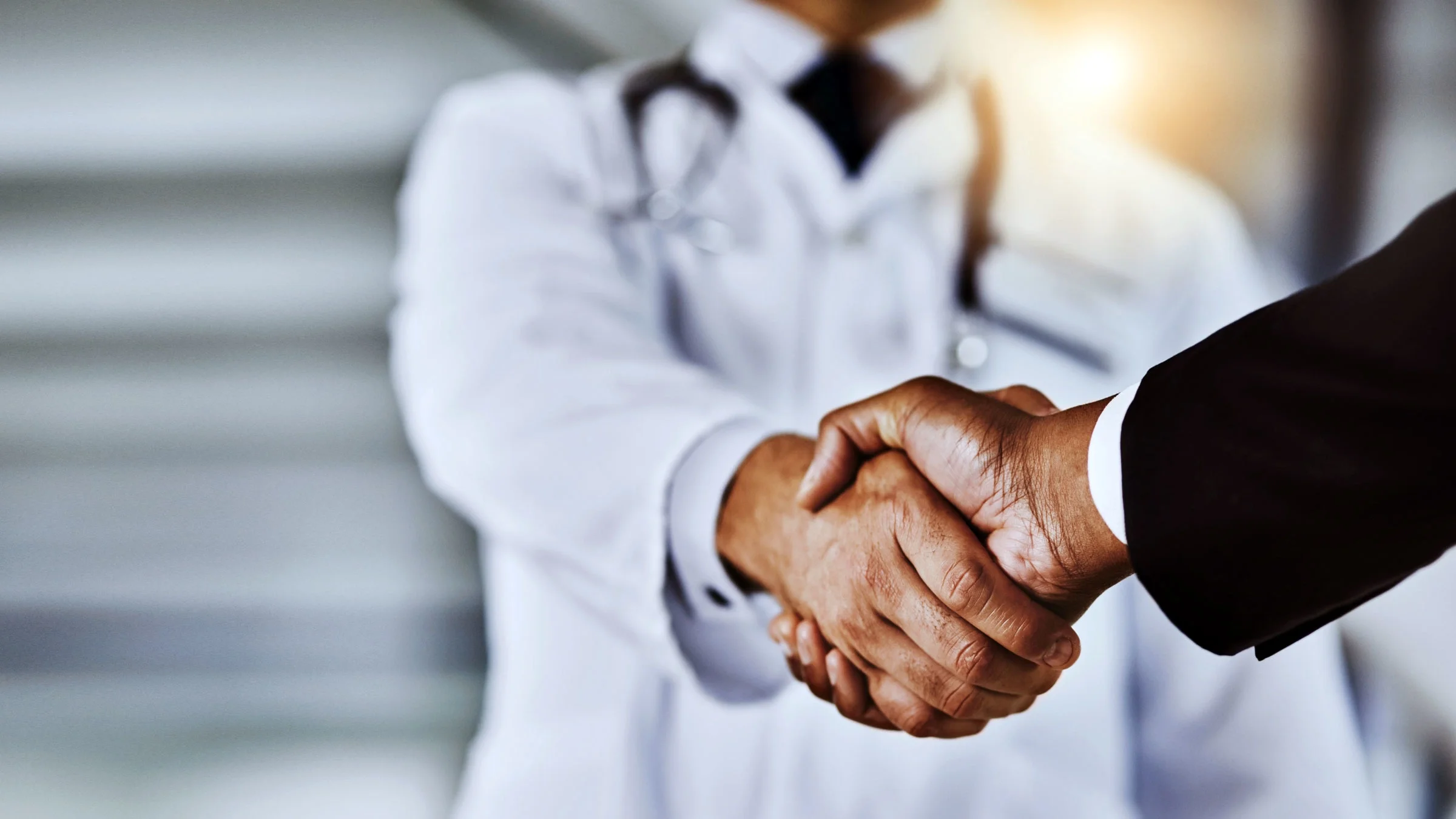 Close-up shot of a doctor shaking hands with a businessman in a hospital.