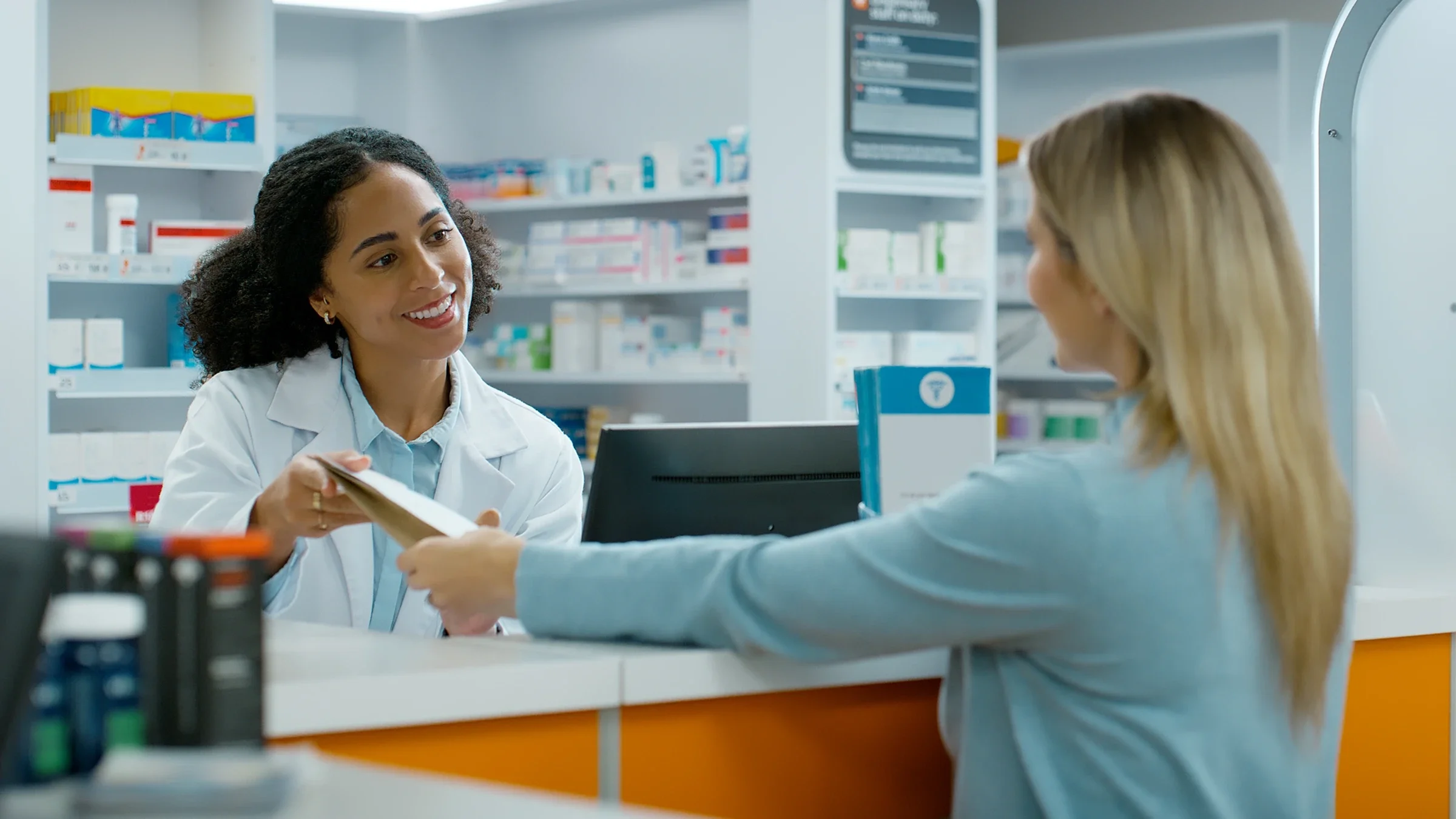A woman talks with an employee at a pharmacy counter.