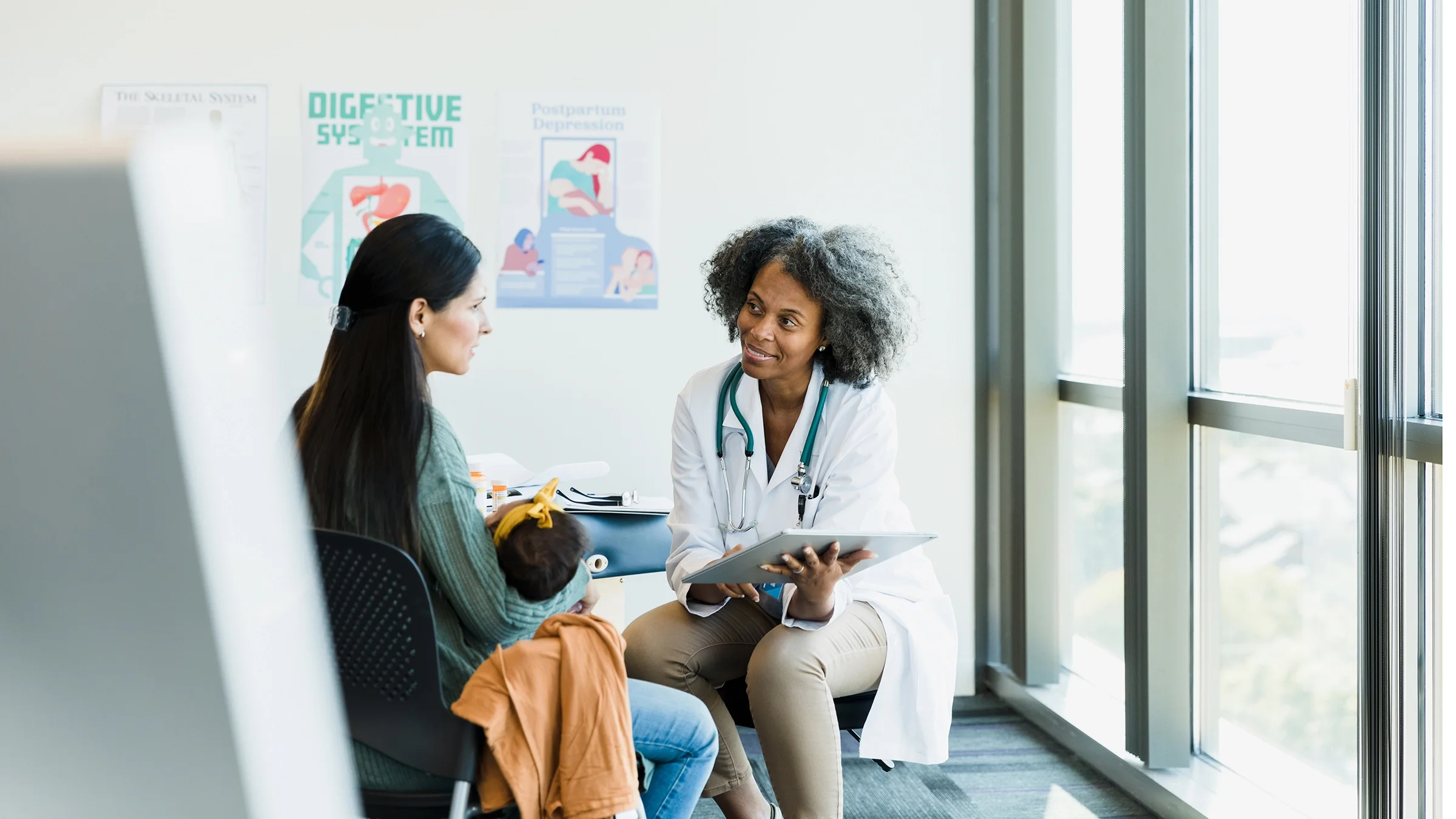 Doctor meeting with a mother and child in a brightly lit exam room.