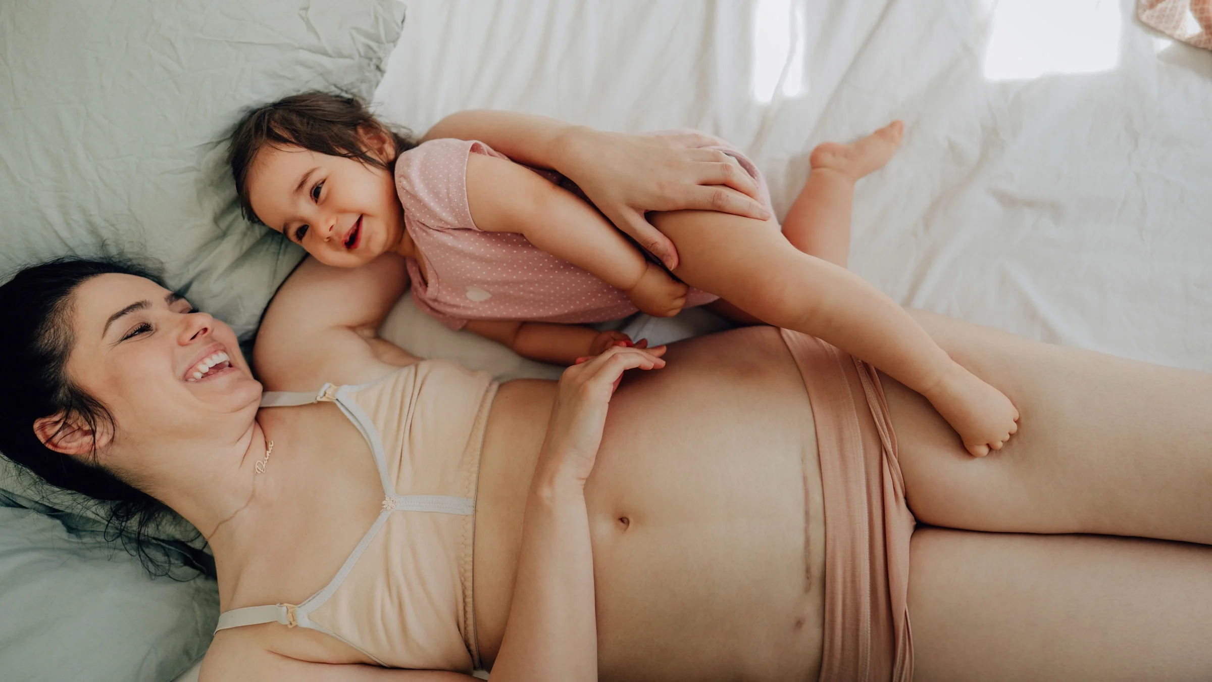 A parent with a C-section scar cuddling in bed with their child.