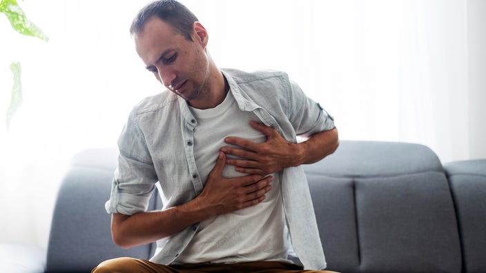 A man grabs his chest while sitting on a couch.