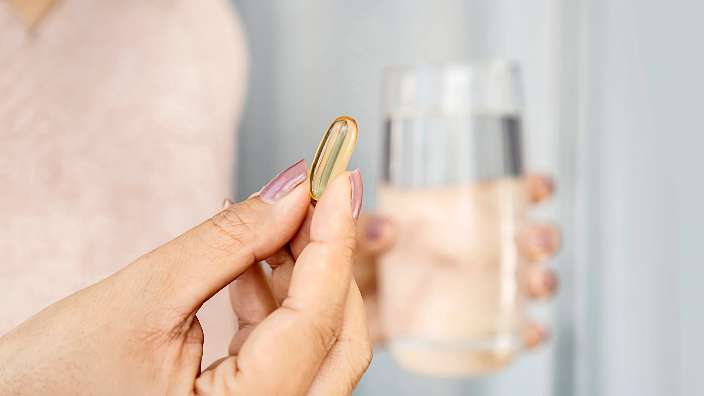 Close-up hand holding capsule pill with a glass of water.