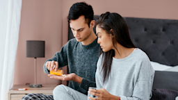 A couple in pajamas sitting on a bed. The main is taking a pill.
PeopleImages/iStock via Getty Images Plus 