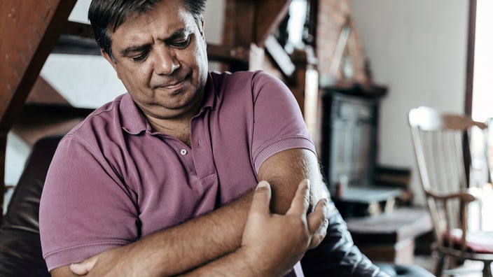 Man grabbing elbow in pain. He is wearing a light red polo shirt.