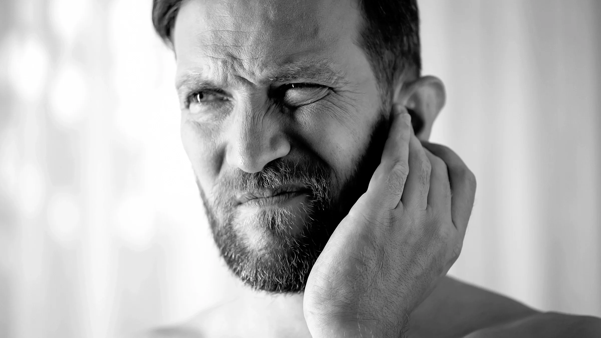 Black and white close-up of a man with an ear infection. He has a scrunched looked on his face like he is in pain.