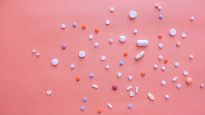 Pills scattered on a pink background.