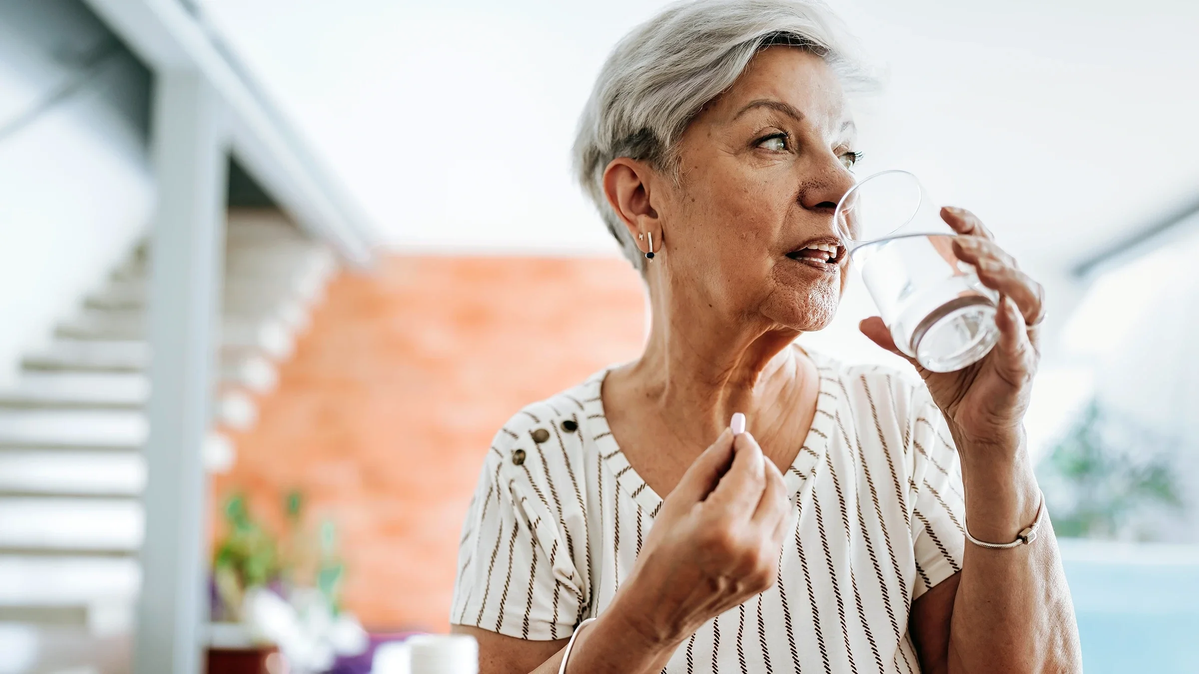 A woman takes an oral pill with a glass of water.